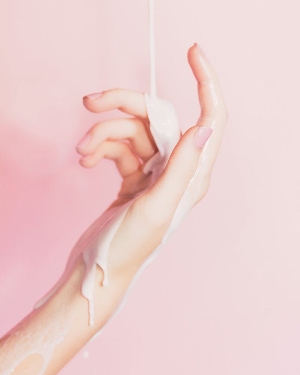 Main sous un filet de lait sur fond rose